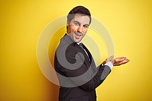 Young handsome businessman wearing suit and tie standing over isolated yellow background pointing aside with hands open palms