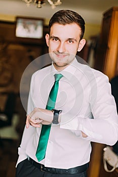 Young handsome businessman in white shirt with green tie checking time looking on his watch