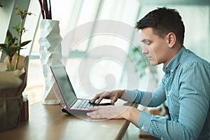 Young handsome businessman works in his laptop while having lunch in cafe near office