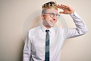 Young handsome caucasian business man wearing golden crown over isolated background very happy and smiling looking far away with