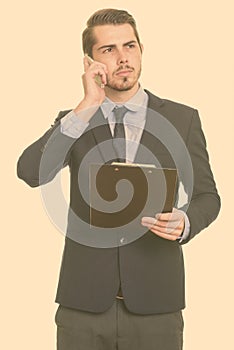Young handsome Caucasian businessman talking on mobile phone while holding cipboard