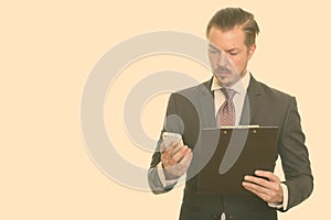 Young handsome Caucasian businessman using mobile phone while holding clipboard