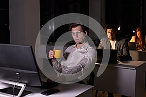 young handsome caucasian guy drinking coffee and working in office at night
