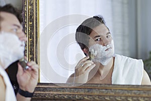 Young handsome caucasian man begins to shave with brush and foam, vintage style of old barber. Thoughtful serious look