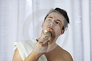 Young handsome caucasian man begins to shave with brush and foam, vintage style of old barber. Thoughtful serious look