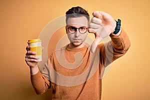 Young handsome caucasian man drinking coffee from a take away thermo bottle with angry face, negative sign showing dislike with