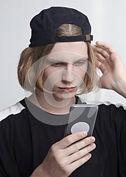 Young handsome caucasian man looks to the mobile phone screen like in mirror, getting up the hairs, or making selfie.