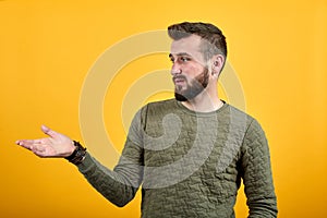 Young handsome caucasian man pointing with palm aside, looking calm