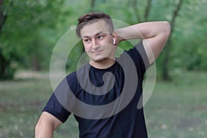 Young handsome caucasian man puts a hand on the neck, complicated expression on the face, smiling.