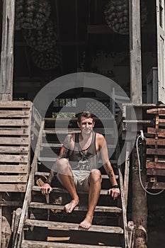 Young handsome caucasian man with a sleeve tattoo sits on the wooden stairs