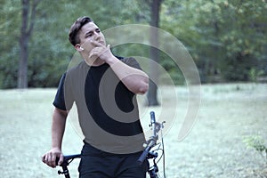 Young handsome caucasian man stands with his bicycle touching face in a model style.