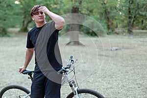 Young handsome caucasian man stands with his bicycle touching his hair in a model style.