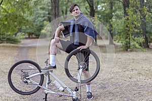 Young handsome caucasian man stands leg on the bicycle in a proudly exhaggerated style. White earphones, casual freak sportswear.