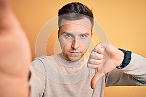 Young handsome caucasian man talking a selfie picture over yellow isolated background with angry face, negative sign showing
