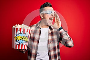 Young handsome caucasian man wearing 3d movie glasses and eating popcorn shouting and screaming loud to side with hand on mouth