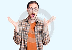 Young handsome caucasian man wearing casual clothes and glasses celebrating victory with happy smile and winner expression with