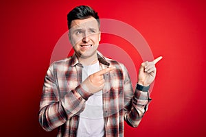 Young handsome caucasian man wearing casual modern shirt over red isolated background Pointing aside worried and nervous with both