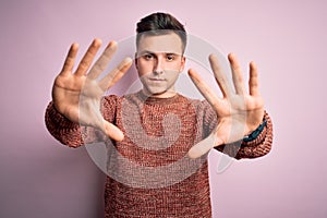 Young handsome caucasian man wearing casual winter sweater over pink isolated background doing frame using hands palms and