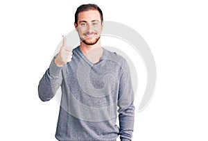 Young handsome caucasian man wearing casual winter sweater smiling happy and positive, thumb up doing excellent and approval sign