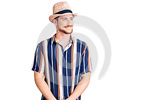 Young handsome caucasian man wearing summer hat looking away to side with smile on face, natural expression
