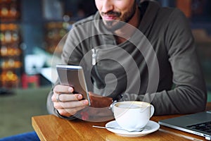 Young handsome cheerful hipster guy at the restaurant using a mobile phone, hands close up. Selective focus. photo