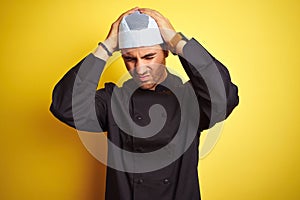 Young handsome chef man cooking wearing uniform and hat over isolated yellow background suffering from headache desperate and