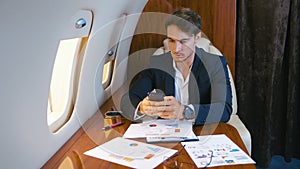 Young handsome chief banker director businessman working using smartphone durung flying in airplane. Successful business