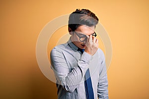 Young handsome chinese businessman wearing glasses and tie over yellow background tired rubbing nose and eyes feeling fatigue and