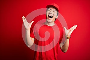 Young handsome chinese delivery man wearing cap standing over isolated red background celebrating mad and crazy for success with