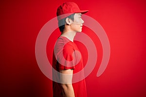 Young handsome chinese delivery man wearing cap standing over isolated red background looking to side, relax profile pose with