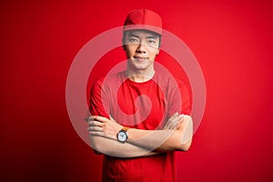 Young handsome chinese delivery man wearing cap standing over isolated red background skeptic and nervous, disapproving expression