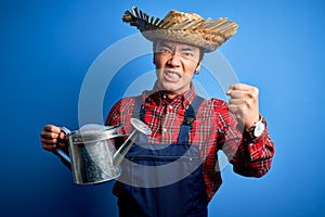 Young handsome chinese farmer man wearing apron and straw hat holding watering can annoyed and frustrated shouting with anger,