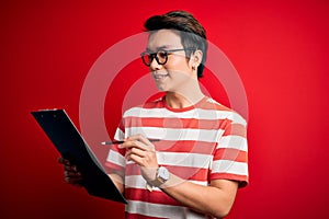 Young handsome chinese inspector man wearing glasses holding clipboard checklist with a happy face standing and smiling with a