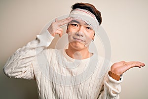 Young handsome chinese man injured for accident wearing bandage and strips on head confused and annoyed with open palm showing