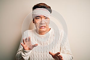 Young handsome chinese man injured for accident wearing bandage and strips on head disgusted expression, displeased and fearful