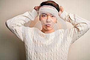 Young handsome chinese man injured for accident wearing bandage and strips on head doing funny gesture with finger over head as
