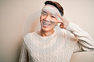 Young handsome chinese man injured for accident wearing bandage and strips on head Doing peace symbol with fingers over face,