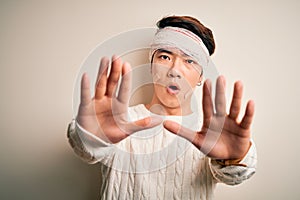 Young handsome chinese man injured for accident wearing bandage and strips on head doing stop gesture with hands palms, angry and