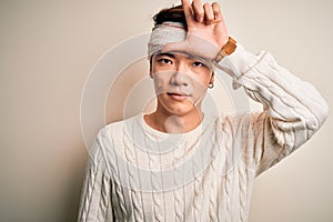 Young handsome chinese man injured for accident wearing bandage and strips on head making fun of people with fingers on forehead