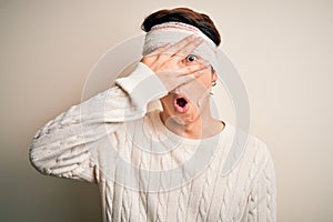 Young handsome chinese man injured for accident wearing bandage and strips on head peeking in shock covering face and eyes with