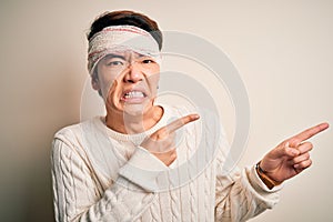 Young handsome chinese man injured for accident wearing bandage and strips on head Pointing aside worried and nervous with both