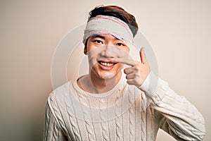 Young handsome chinese man injured for accident wearing bandage and strips on head Pointing with hand finger to face and nose,