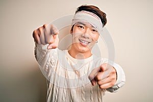 Young handsome chinese man injured for accident wearing bandage and strips on head pointing to you and the camera with fingers,