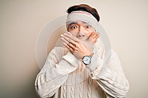 Young handsome chinese man injured for accident wearing bandage and strips on head shocked covering mouth with hands for mistake