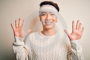 Young handsome chinese man injured for accident wearing bandage and strips on head showing and pointing up with fingers number ten