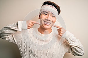 Young handsome chinese man injured for accident wearing bandage and strips on head smiling cheerful showing and pointing with