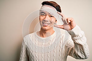 Young handsome chinese man injured for accident wearing bandage and strips on head smiling and confident gesturing with hand doing