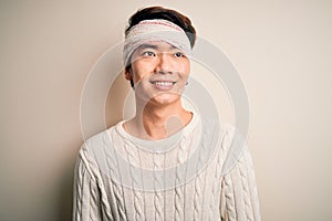 Young handsome chinese man injured for accident wearing bandage and strips on head smiling looking to the side and staring away