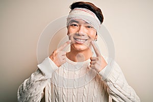 Young handsome chinese man injured for accident wearing bandage and strips on head Smiling with open mouth, fingers pointing and
