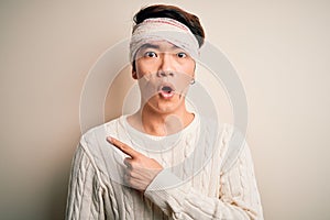 Young handsome chinese man injured for accident wearing bandage and strips on head Surprised pointing with finger to the side,